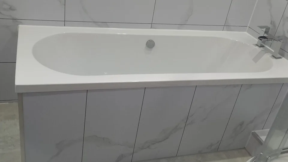 White fitted bath with marble-effect panel and walls